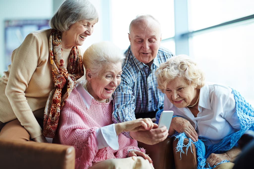 Four older adults smiling over a smartphone