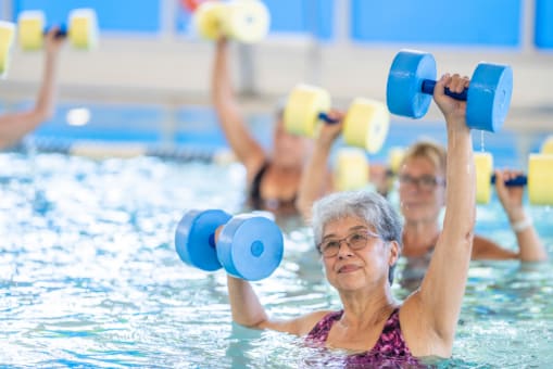 Older women doing water aerobics with foam dumbbells
