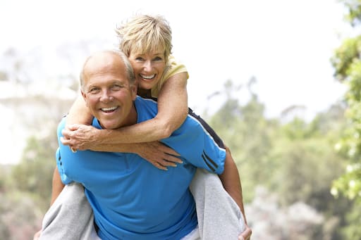 Smiling older couple outdoors, with the woman riding piggyback