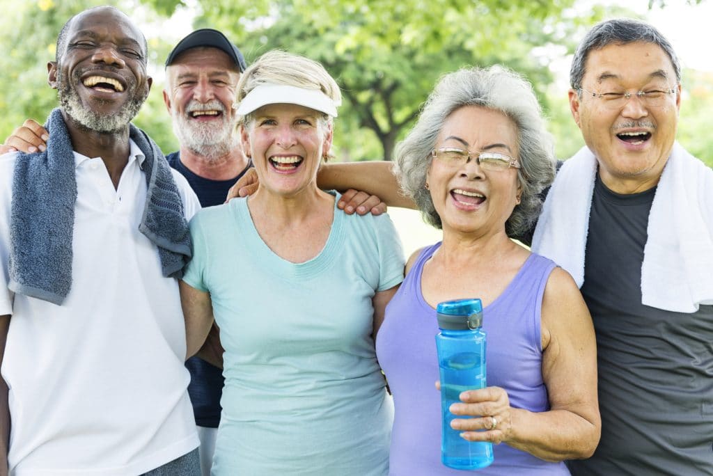 Five older adults in exercise clothes smiling outdoors
